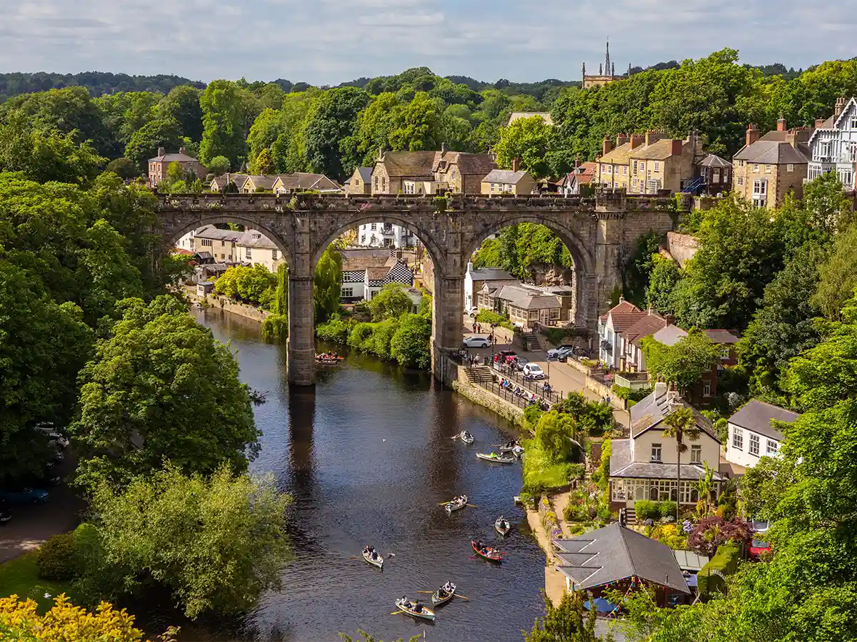 Picturesque view of the River Nidd and the iconic Knaresborough Viaduct in North Yorkshire, surrounded by lush greenery and charming riverside buildings.