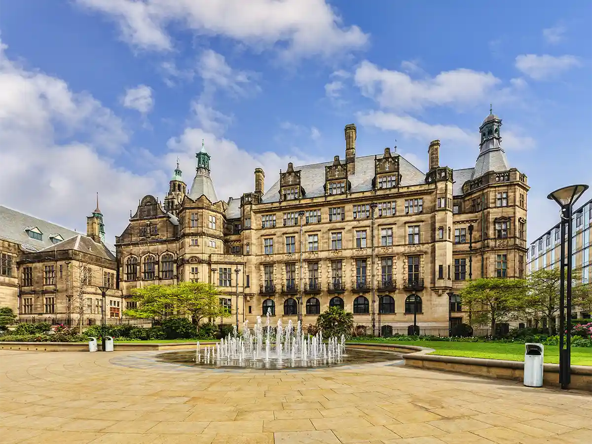 Historic building in Sheffield, South Yorkshire, with ornate architecture and a fountain in the foreground, set against a clear blue sky.