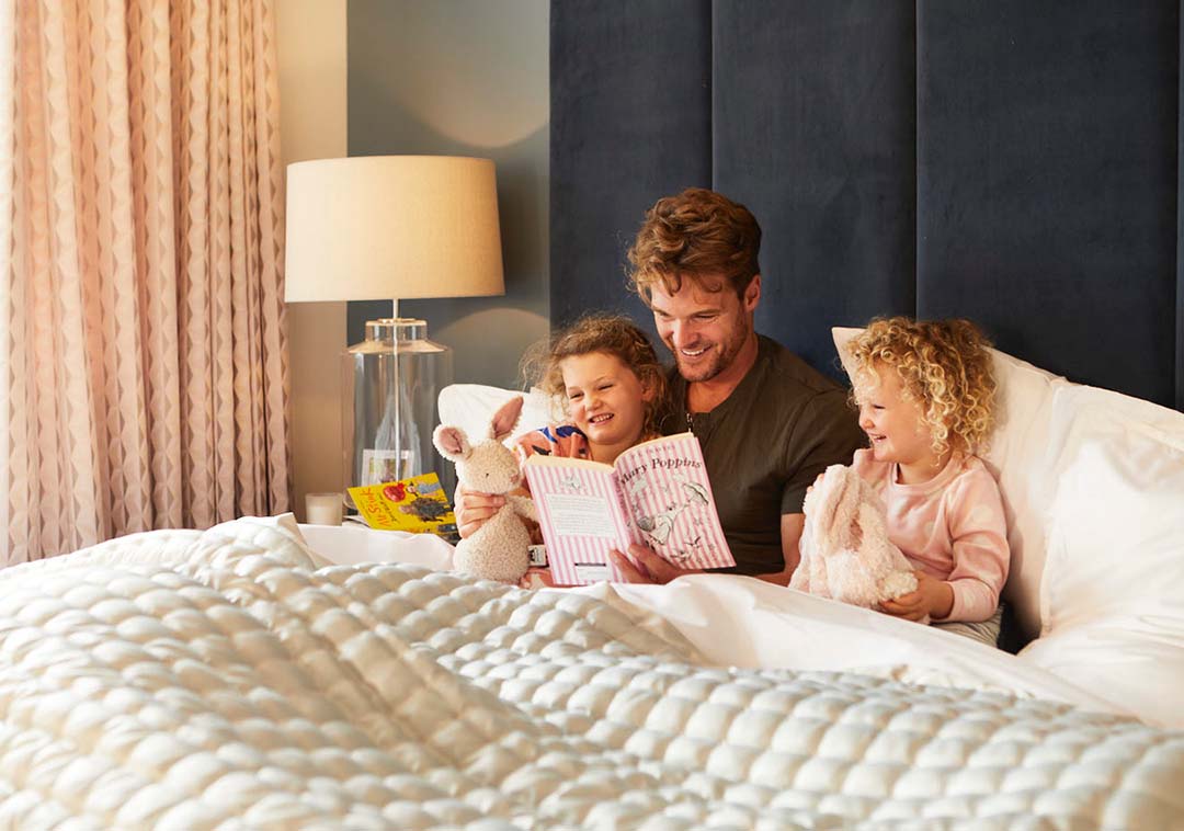 A father sitting in bed with his daughters reading a bedtime story